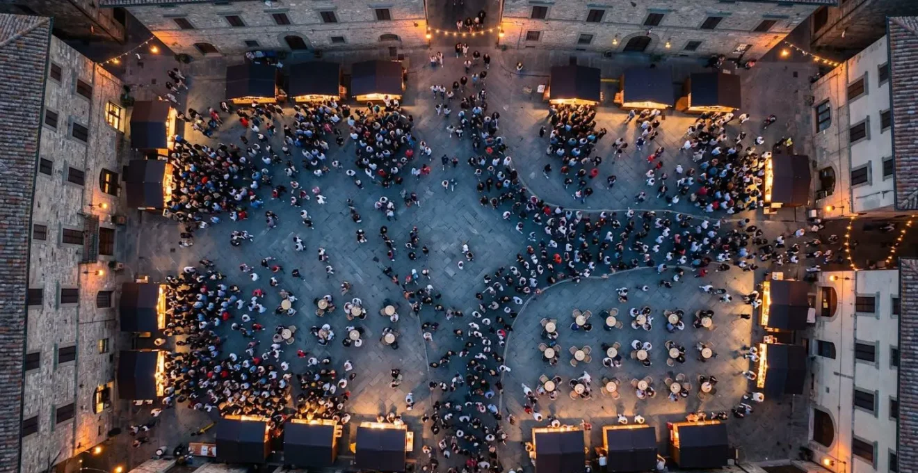 Vista aerea di una piazza di paese durante una sagra con diversi gruppi di persone in movimento