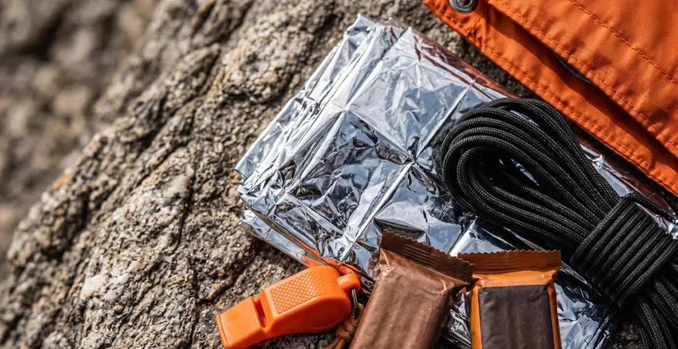 Kit di emergenza da montagna disposto su roccia con telo termico e attrezzatura di sicurezza